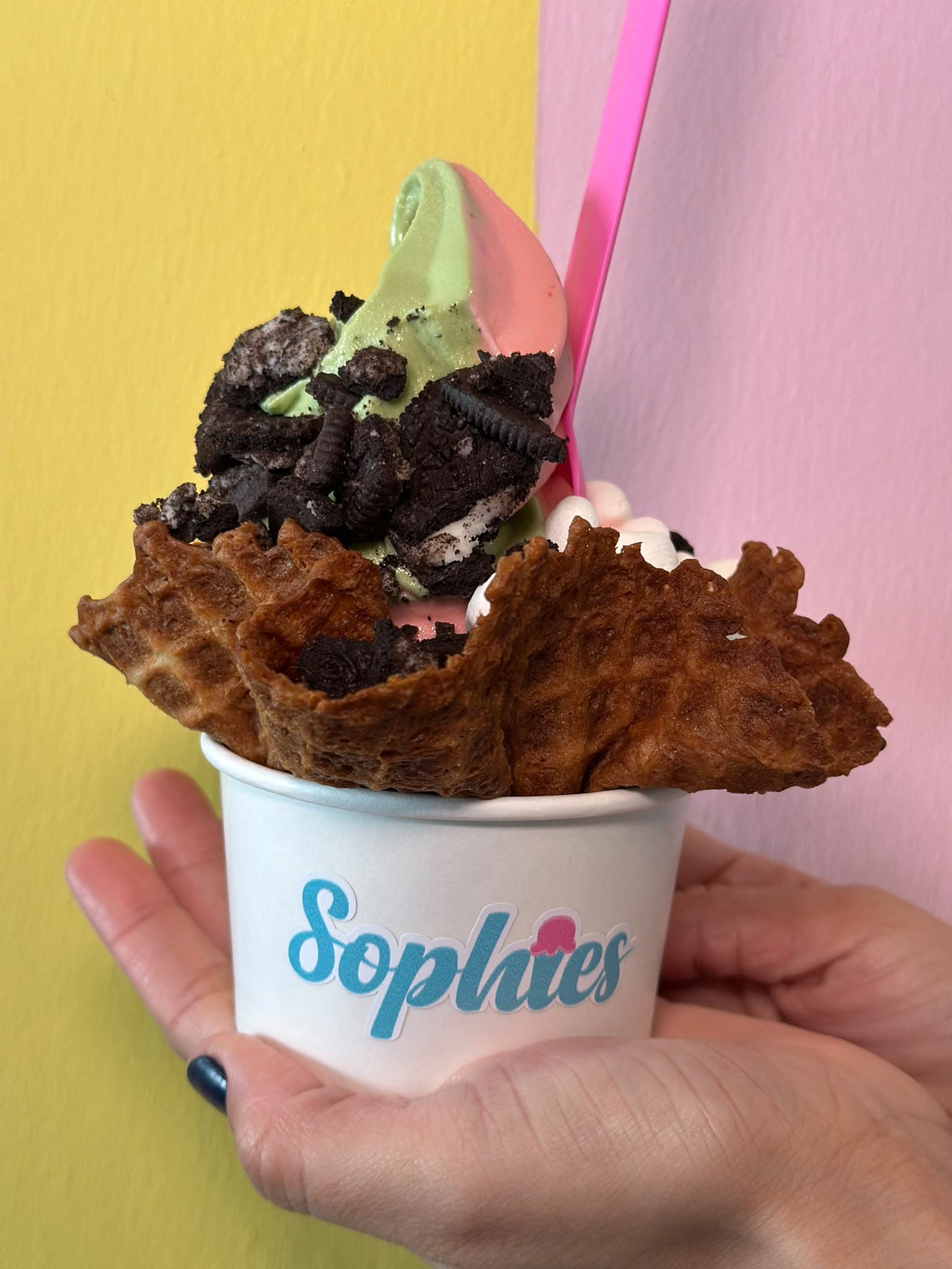 Primer plano de una mezcla de matcha y fresa en un tazón de waffle con trocitos de Oreo y marshmallows en un vaso de Sophie’s